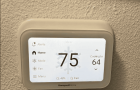 Ductless Mini Split Maintenance Checklist: Your Seasonal Guide An image showing a white Honeywell Home smart thermostat mounted on a textured, beige wall. The thermostat's screen is lit, displaying the current indoor temperature as 75 degrees in large black numbers with a faint snowflake icon behind them. On the right, it shows "Cooling to 64" with up and down arrows. The left side of the screen features a menu with options for Alerts, Home, Mode, Fan, and Menu. At the bottom, it indicates 48% humidity and "Fair" air quality.